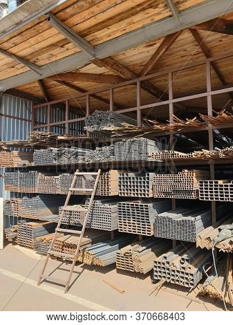 Construction Market. Racks With Metal Rods And Profiles With A Ladder Attached To Them