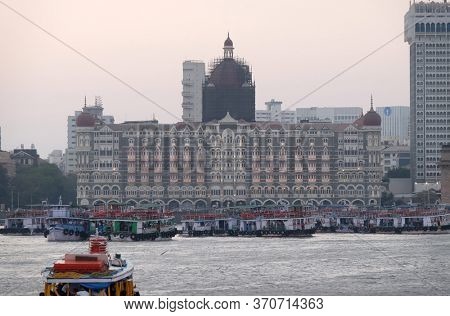 MUMBAI, INDIA - FEBRUARY 15, 2020: Taj Mahal hotel, Gateway of India and tourist boats in water of Arabian Sea in Mumbai, India