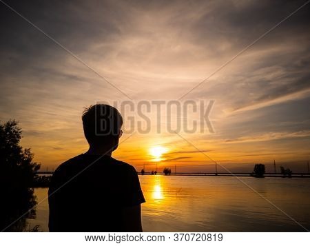 Silhouette Of A Man With A Short Haircut On The Background Of The Lake In The Light Of The Setting S