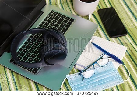 Laptop, Notepad, Pen, Gadgets, Glasses, Medical Mask, Tea Cup. Close-up Comfortable Workplace. Remot