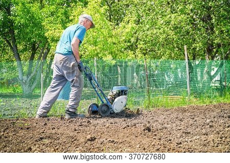 A Man Cultivates The Soil In The Garden Using A Motor Cultivator - Tiller