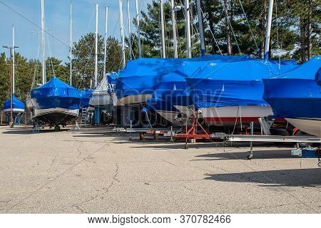 Row Of Sailboats With Blue Shrink Wrap Covers In Outdoor Storage Lot