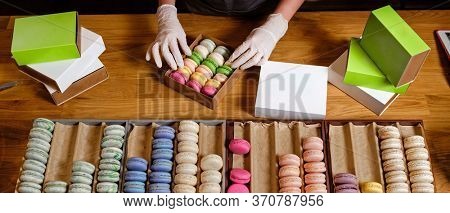 Female hands in gloves packs traditional french dessert macaroon in paper boxes for delievery