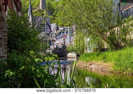 The Village Monreal With River Elz, Half-timbered Houses And Castle Loewenburg In The Background