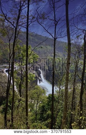 A Landscape Of A Waterfall Behind Trees Located In Athirapally Located In Kerala State, India