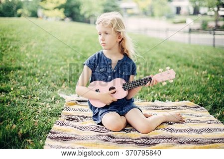 Cute Adorable Blonde Girl Playing Pink Guitar Toy Outdoor. Child Playing Music And Singing Song In P