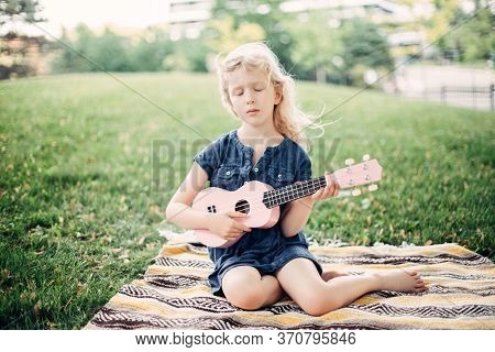 Cute Adorable Blonde Girl Playing Pink Guitar Toy Outdoor. Child Playing Music And Singing Song In P