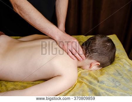 Toddler Relaxes From A Therapeutic Massage. The Hands Of A Masseur