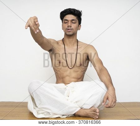 Young Indian Priest Sitting In Dhoti, Wearing Rudraksh, Showing Up His Hand Representing Giving Shou