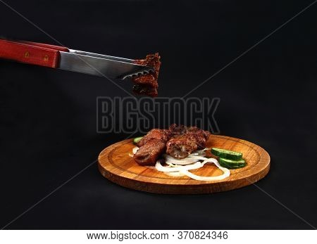 Shashlick And Cut Vegetables On Wooden Cutting Board On Black Background. One Piece Of Meat Held Wit
