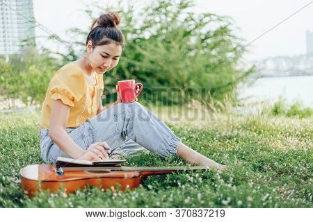 Hands Hold Coffee Cup And Write Notes,lyrics In The Book On Quitar Beside The Sea And Building City 