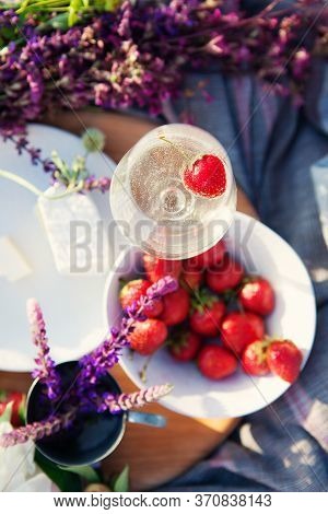 Picnic In Grass, Cheese, Strawberries, Wildflowers, Glass Of Champagne On Wooden Board.