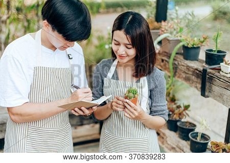 Women Hold Cactus And A Man Writing Note In A Book. Love Couple Enjoy Hobby With Darden Cactus.