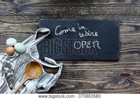 Baking Supplies With Apron, Whisk, Measuring Spoons And Eggs Beside Of A Sign That Reads, 