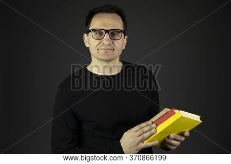Pensive Academic Professor In Casual Black Wear And Glasses Holding Books In Hands And Looks At Came