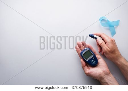 Digital Blood Glucose Meter, Lancet Pen In Male Hands On A Gray Background With A Blue Ribbon, Flat 
