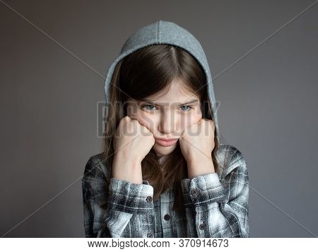 Portrait Of A Little Sad Girl In A Hoodie On A Dark Background