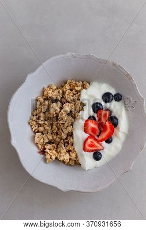 Topview Image Of Granola With Yogurt, Strawberries And Berries In A White Rustic Bowl Over Light Gra