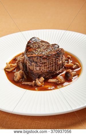 Filet mignon served with mushrooms side view. Beef steak on white plate close-up. Luxury restaurant delicious main course. Fancy roasted meat dish with sauce closeup. Gourmet meal