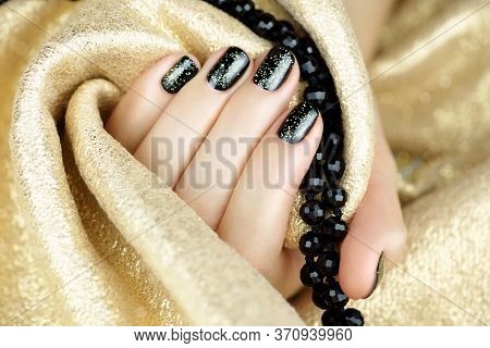 Female Hand With Black Manicure And Gold Sparkles On A Golden Background