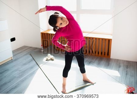 Little Girl Is Doing Back Tilt Standing Workout At Home. Cute Kid Is Training Onon A Mat Indoor Indo