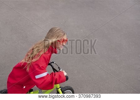 Young Blonde Girl In Red Jacket Riding Bike. Child Bicycle In City. Little Lady Enjoying Bike Ride O