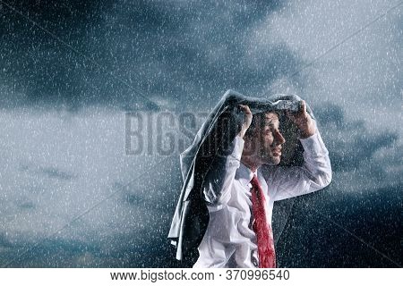 Businessman covering head with jacket during rainstorm