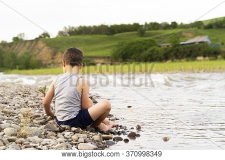 A Village Boy On The River Bank Collects Stones.