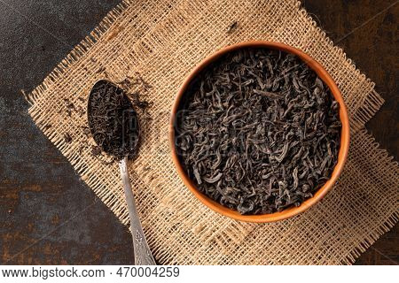 Dry Black Tea Leaves In A Clay Bowl And A Vintage Spoon On A Dark Wooden Background Top View. Large-