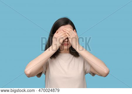 Portrait Of A Serious Student Girl With Glasses, Covering Her Eyes With Her Hands On A Blue Backgrou