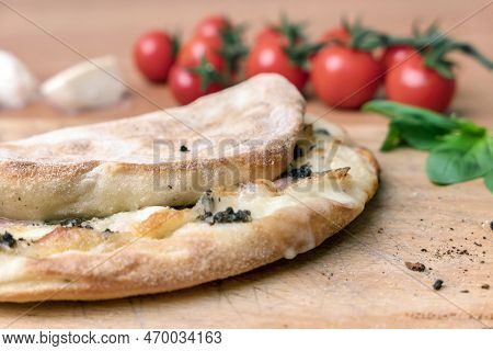 Italian Food, Closed Calzone Pizza On Rustic Wooden Background. On Blurred Background Small Red Toma