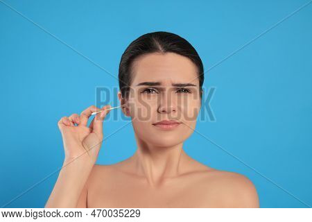 Young Woman Cleaning Ear With Cotton Swab On Light Blue Background