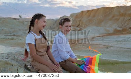 A Boy And A Girl 8-9 Years Old With A Kite Are Having Fun Talking On The Mountain.