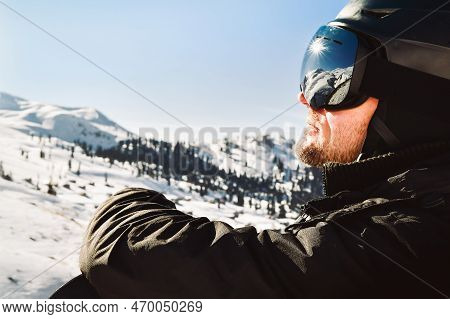 Close Up Of The Ski Goggles Of Caucasian Man With The Reflection Of Snowed Mountains And Sunburst. A