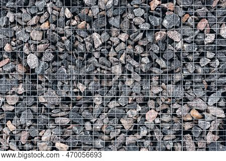 Stone Wall Made Of Whetstone In Light Gray, Enclosed Behind A Metal Mesh. Mineral Surface Without Mo