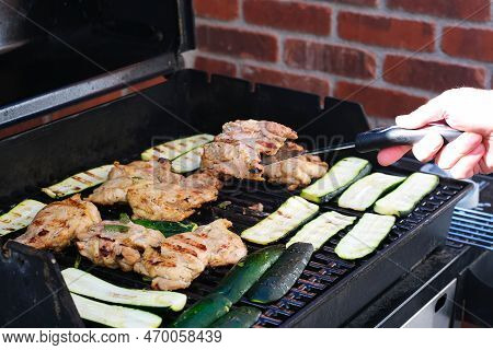 Grilled Chicken And Zukini Vegetables On An Outdoor Barbecue Grill With A Kitchen Spatula In Hand. F