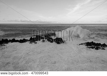 Black And White Photo. The Waves Crash Against Rocks In The Ocean