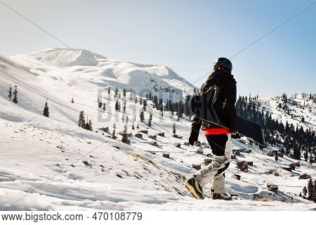 Male Snowboarder Dressed In Dark Black Sportswear Walk Enjoy Views Panorama Of Old Buildings Down Th