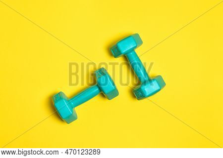 Two Bright Blue Or Mint Dumbbells Are Isolated On Yellow Background. Sport And Health Concept