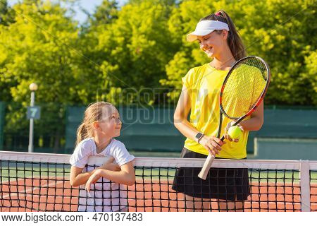 Cheerful Coach In Sports Clothing Teaching Child To Play Tennis While Both Standing On Tennis Court.