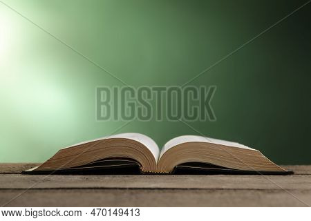 Open Bible On Wooden Table Against Green Background. Space For Text