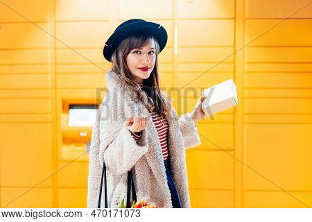 Portrait Of Smiling Fashion Woman With Box Near Modern Postal Automatic Mail Terminal With Self Serv