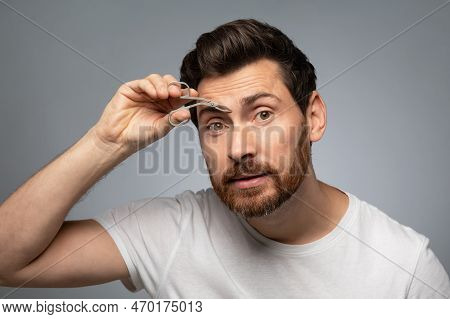 Grooming Wellness And Facial Care. Handsome Middle Aged Bearded Man Tweezing Eyebrows, Grey Backgrou