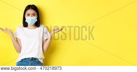 Covid-19, Quarantine And Social Distancing Concept. Confused Asian Woman In Medical Mask Shrugging S
