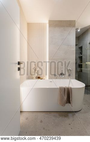 Modern Bright Bathroom With Lamella Wall. Big White Bath With Silver Faucet And Brown Towel.