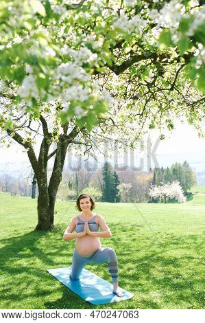 Outdoor Portrait Of Happy Young Pregnant Woman Practicing Youga In Spring Garden Under Blooming Appl