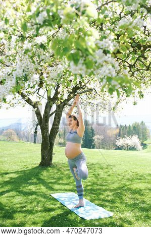 Outdoor Portrait Of Happy Young Pregnant Woman Practicing Youga In Spring Garden Under Blooming Appl