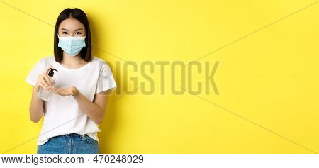 Covid, Health Care And Pandemic Concept. Cute Asian Woman In Medical Mask Using Hand Sanitizer To Di