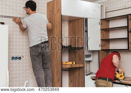 Two Craftsmen, Furniture Makers And Assemblers, Are Installing A Modern Kitchen In A Home, Tools In 