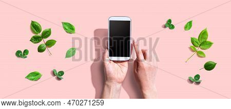 Person Using A Smartphone With Green Leaves - Flat Lay